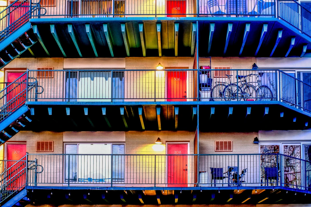 Colorful apartment building facade with stacked blue balconies and vibrant red and yellow door and window frames.