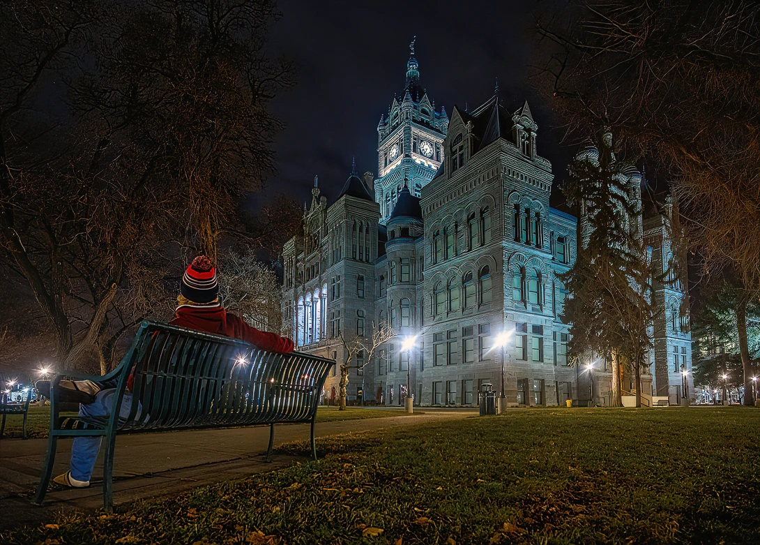 Historic courthouse illuminated at night with a bench in the foreground under bare trees.
