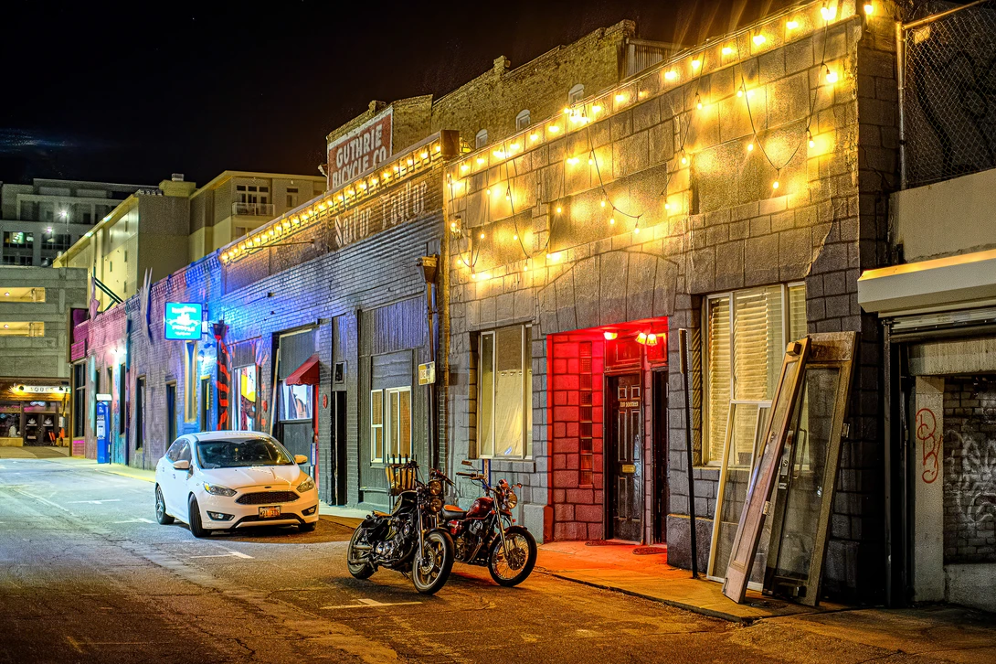Nighttime street scene with illuminated storefront decorated with warm yellow string lights and a red doorway.