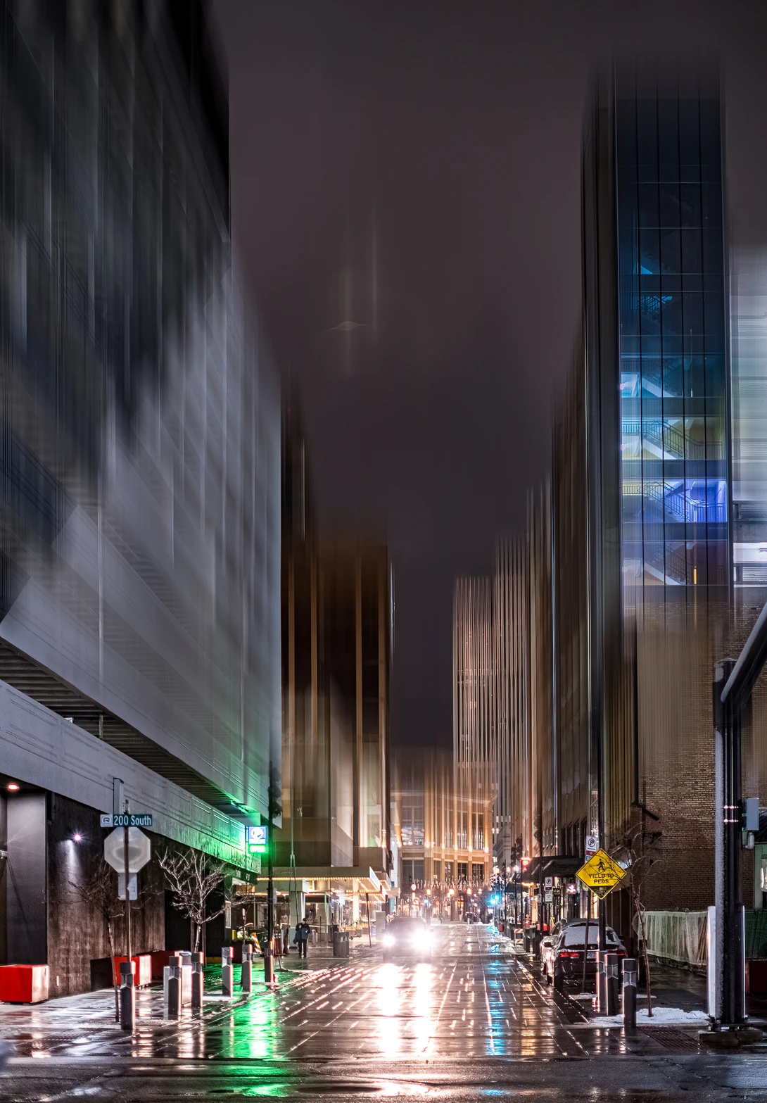 Wet urban street at night with tall buildings rising into fog and mist, lit by street lights and neon signs.
