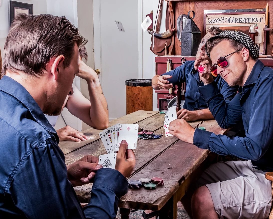 Three men in blue work shirts playing cards at a wooden table in a workshop setting.