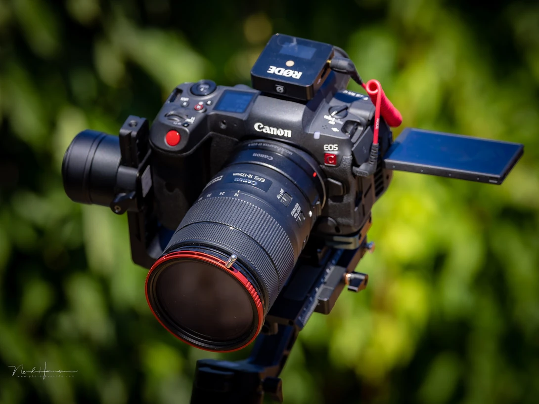 Canon EOS R5C cinema camera with telephoto lens and red accent details mounted on a tripod.