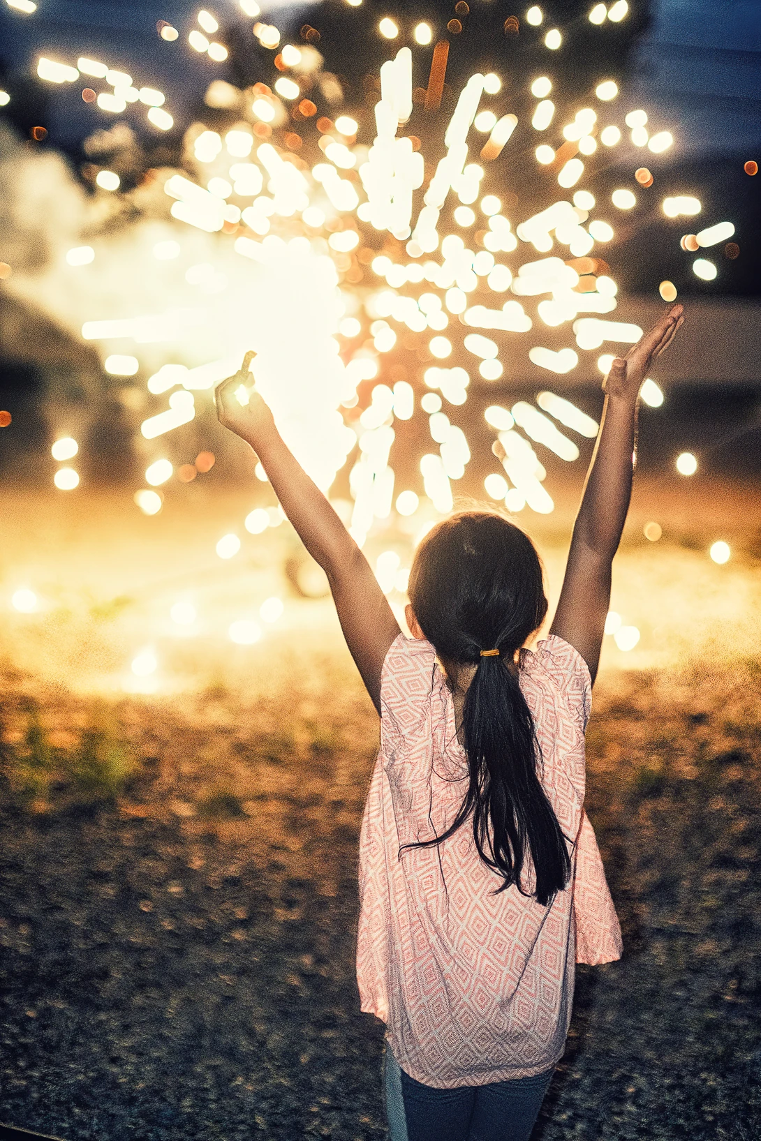 Woman with arms raised toward an explosive burst of golden light against an evening sky.