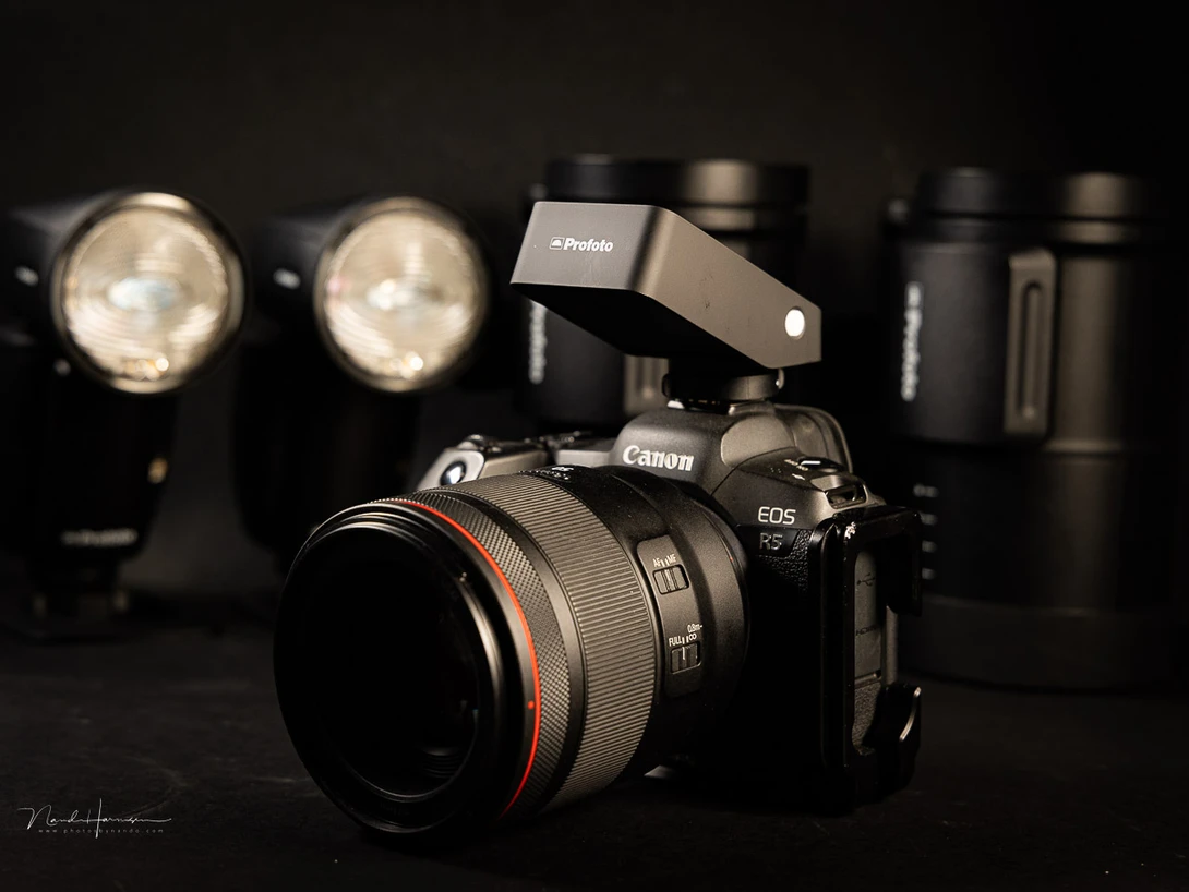 Canon EOS R5 mirrorless camera with RF lens and Godox flash mounted on dark surface surrounded by studio lighting equipment.