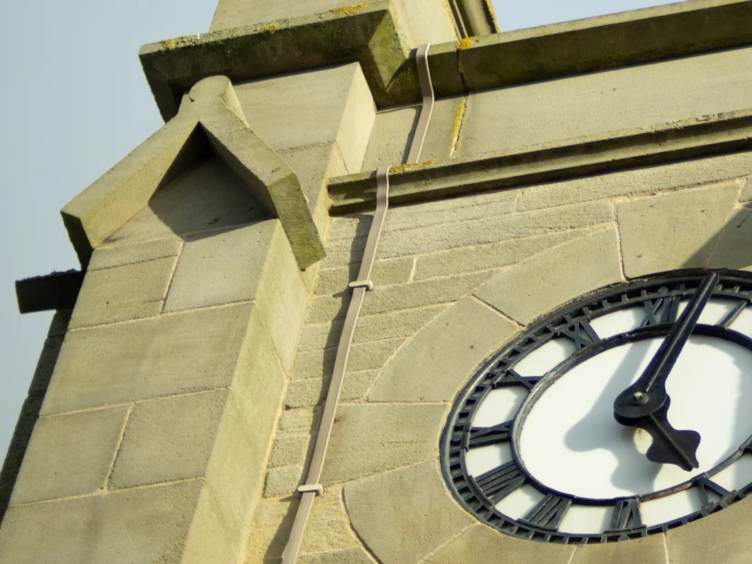 Architectural detail of a stone tower with a clock face and decorative drainpipe.