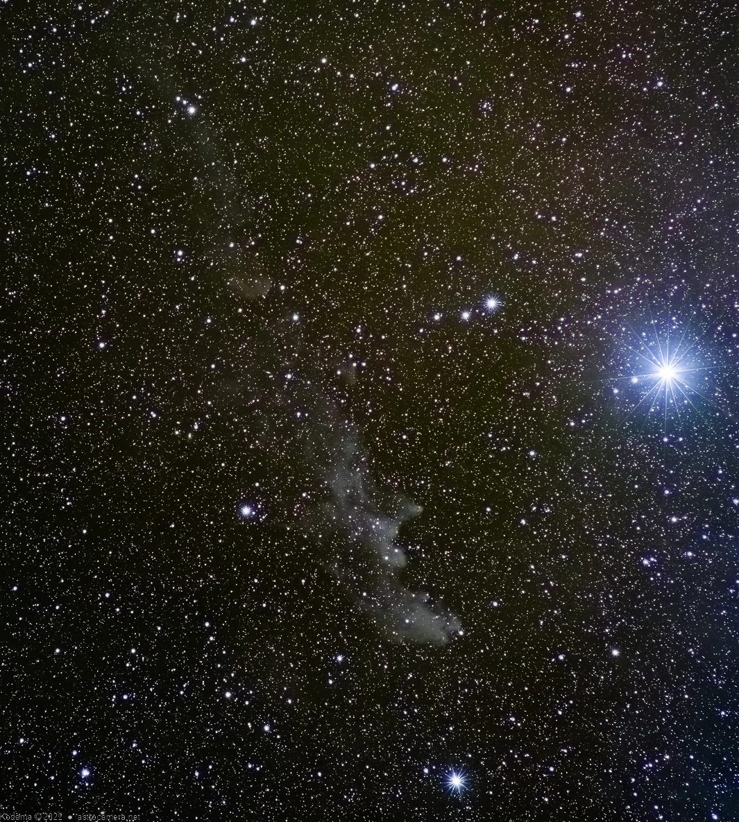 Deep space photograph showing a bright star on the right with a dark nebula cloud formation in the center surrounded by countless distant stars.