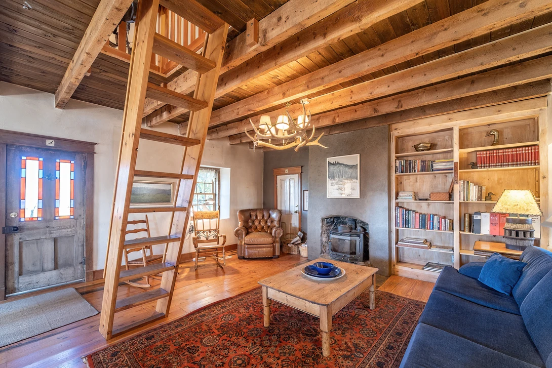 Rustic timber-frame living room with exposed wooden beams, blue sofa, and warm ambient lighting from a chandelier.