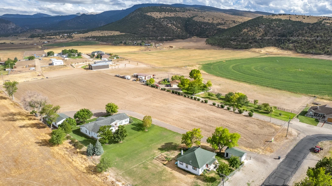 Aerial view of a rural valley with scattered farmhouses, green fields, and forested hills under partly cloudy skies.
