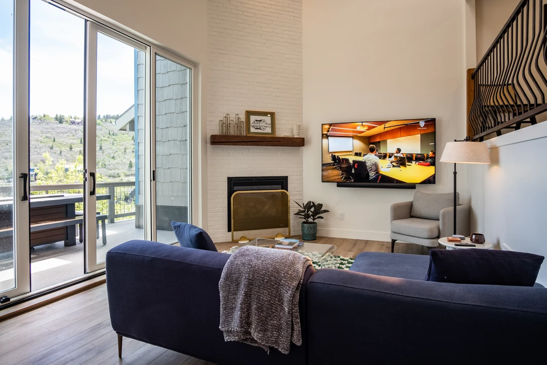 Modern living room with navy curved sofa, fireplace, and large windows overlooking hillside landscape.