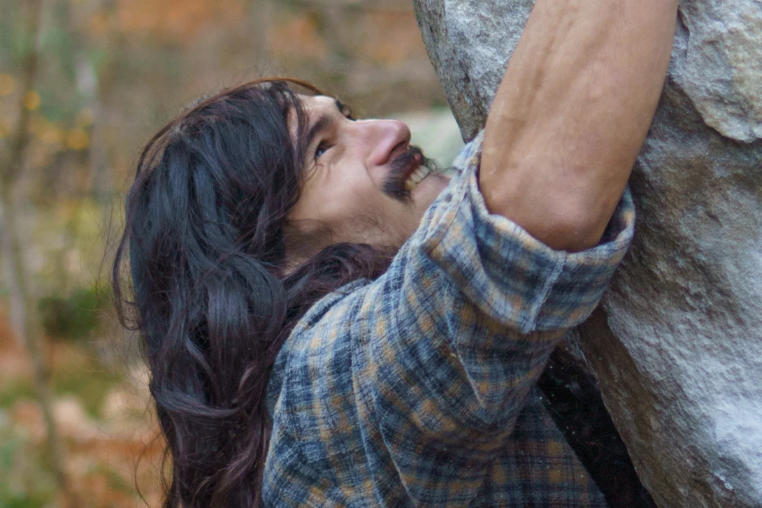 Woman rock climbing outdoors, gripping a textured stone wall with both hands while looking upward.