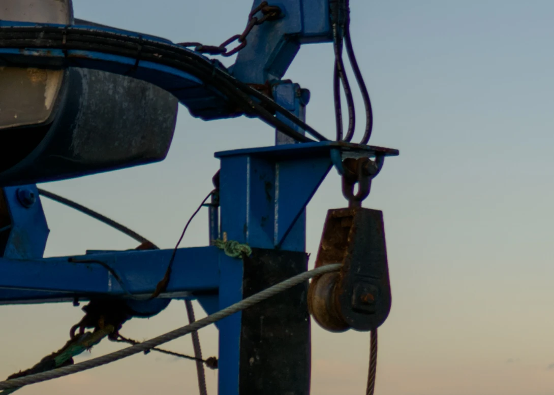 Industrial crane hook and pulley system against a twilight sky.