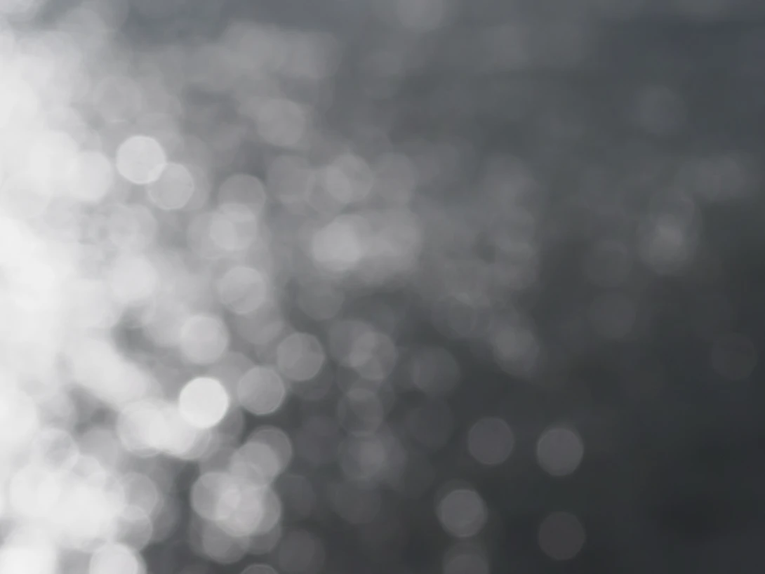 Abstract bokeh effect with soft white and gray circular light blurs fading from bright to dark.