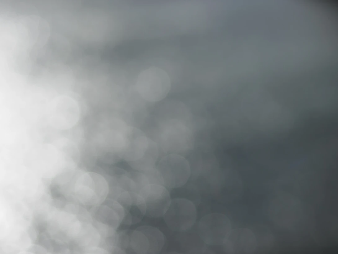 Overexposed bright light creating soft bokeh circles against gray and white cloudy tones.