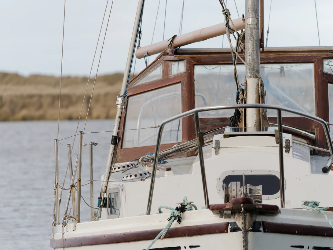 Sailboat moored in calm water with rusty metal boom and rigging visible in foreground.