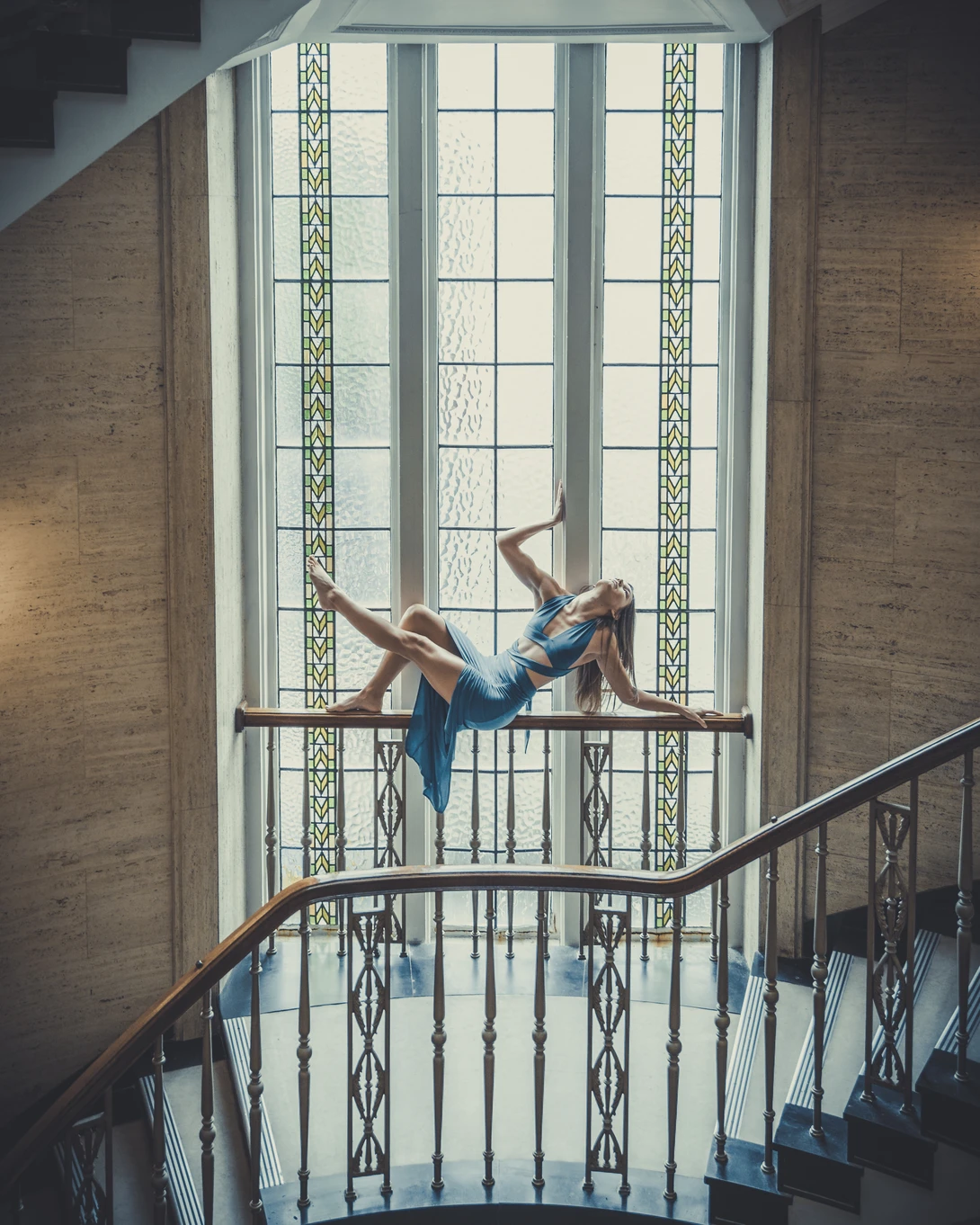 Two people sitting on a railing in front of a large window with geometric patterned panels.