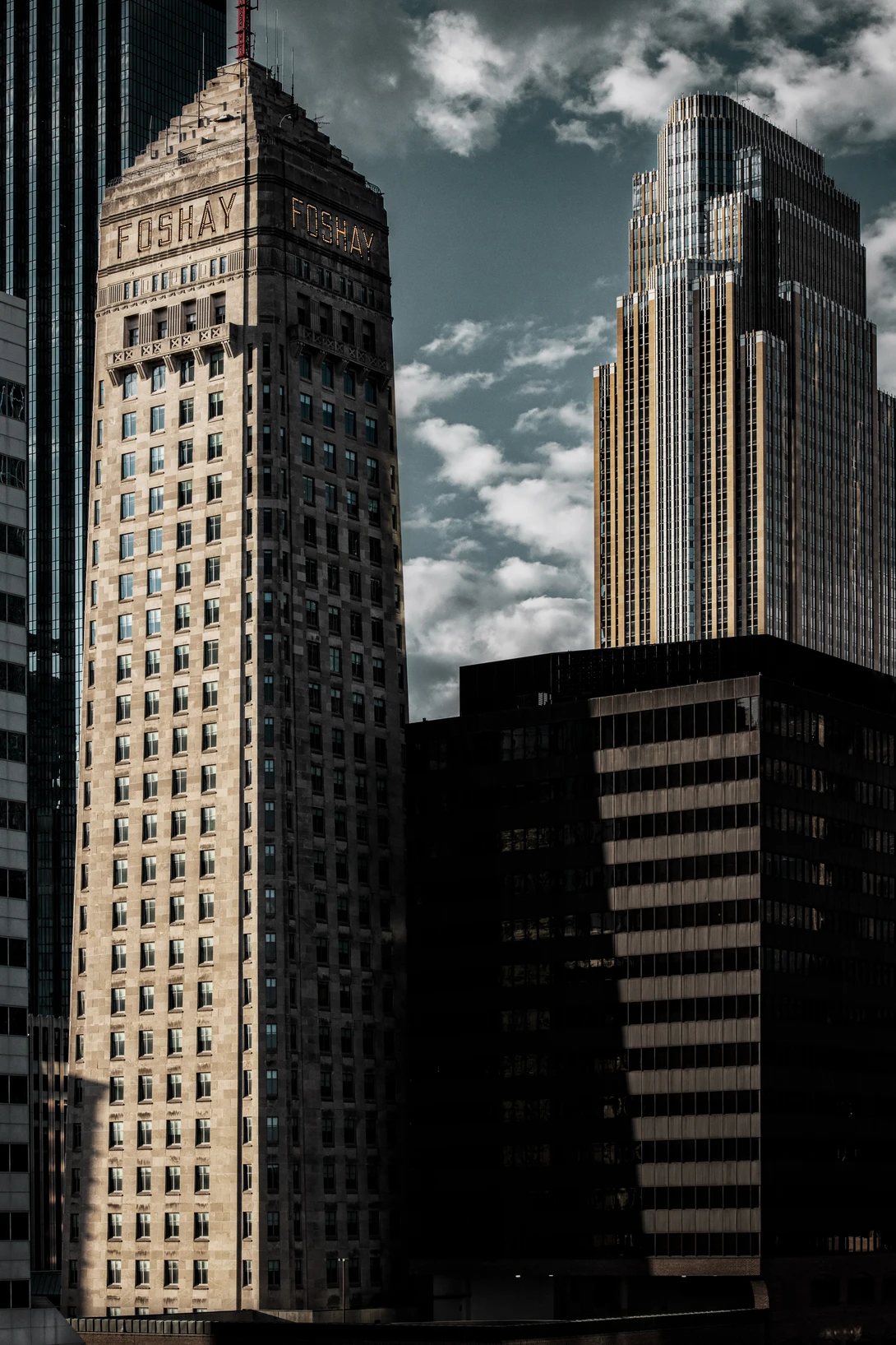 Tall Art Deco skyscraper with limestone facade stands between modern glass buildings under dramatic cloudy sky.