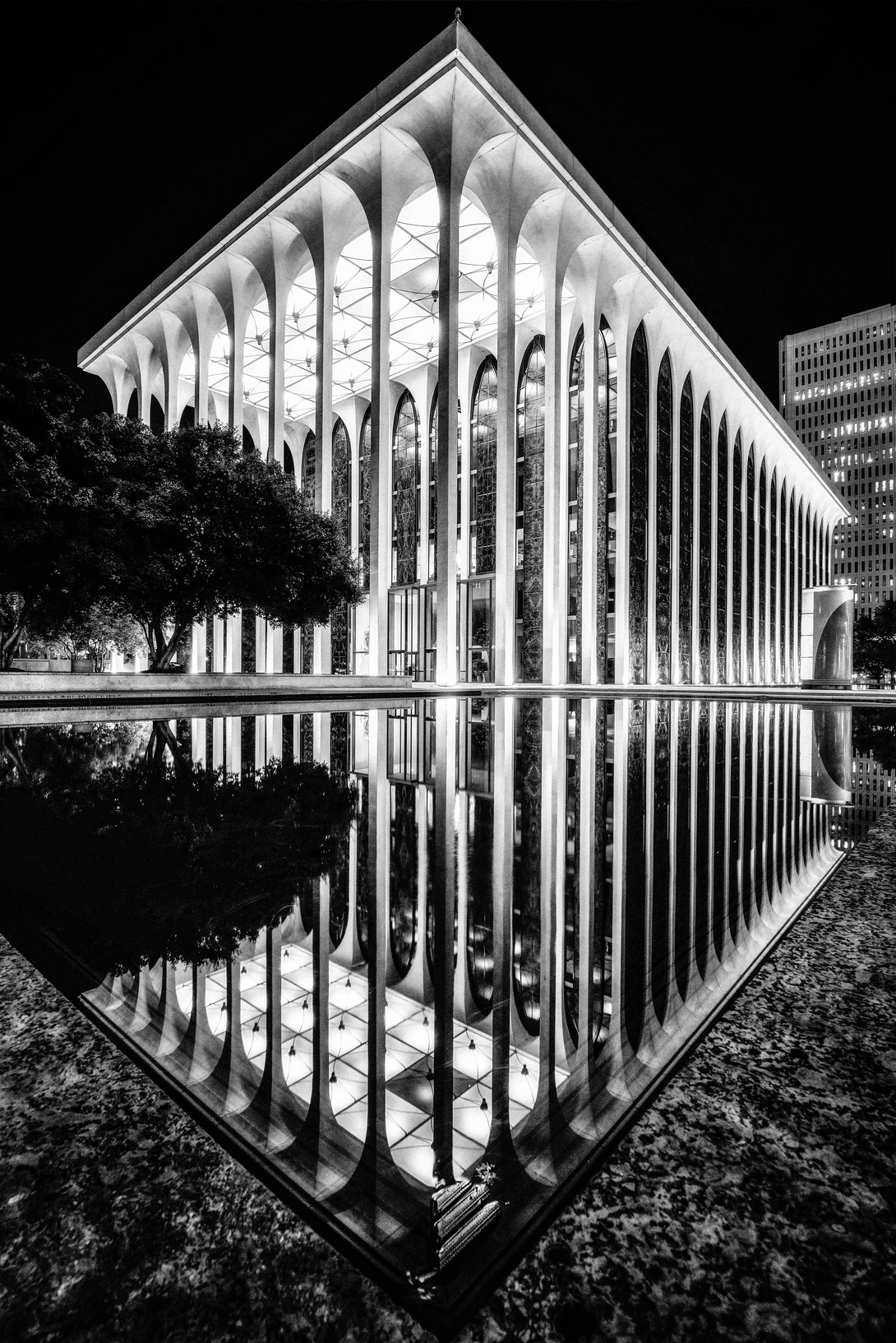 Modern building with ribbed vertical columns reflected in still water at night.