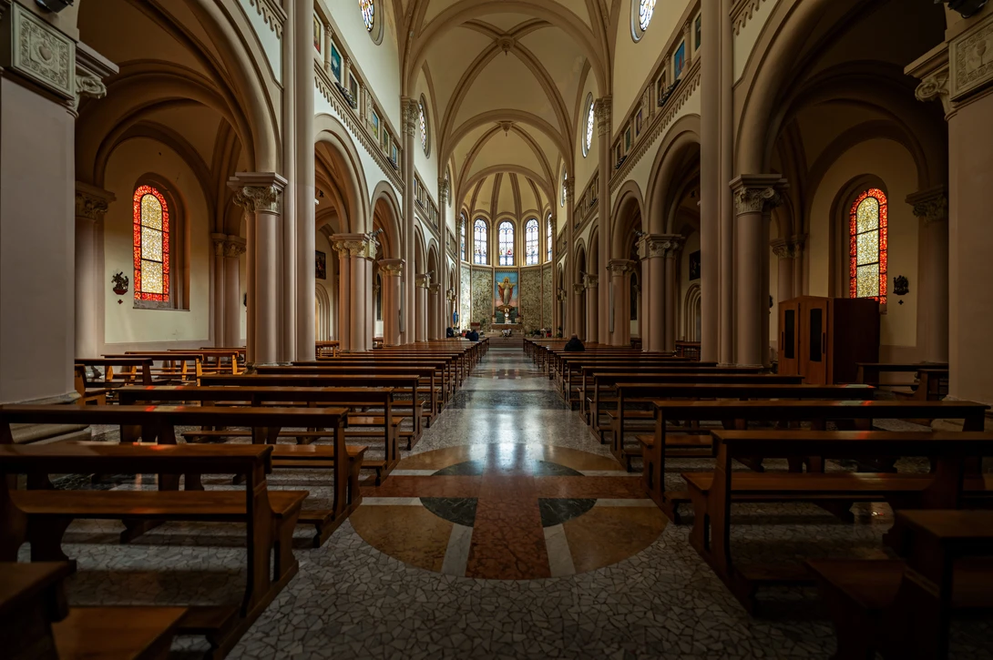 Interior of a Gothic cathedral with soaring vaulted ceilings, wooden pews, and stained glass windows casting warm light.