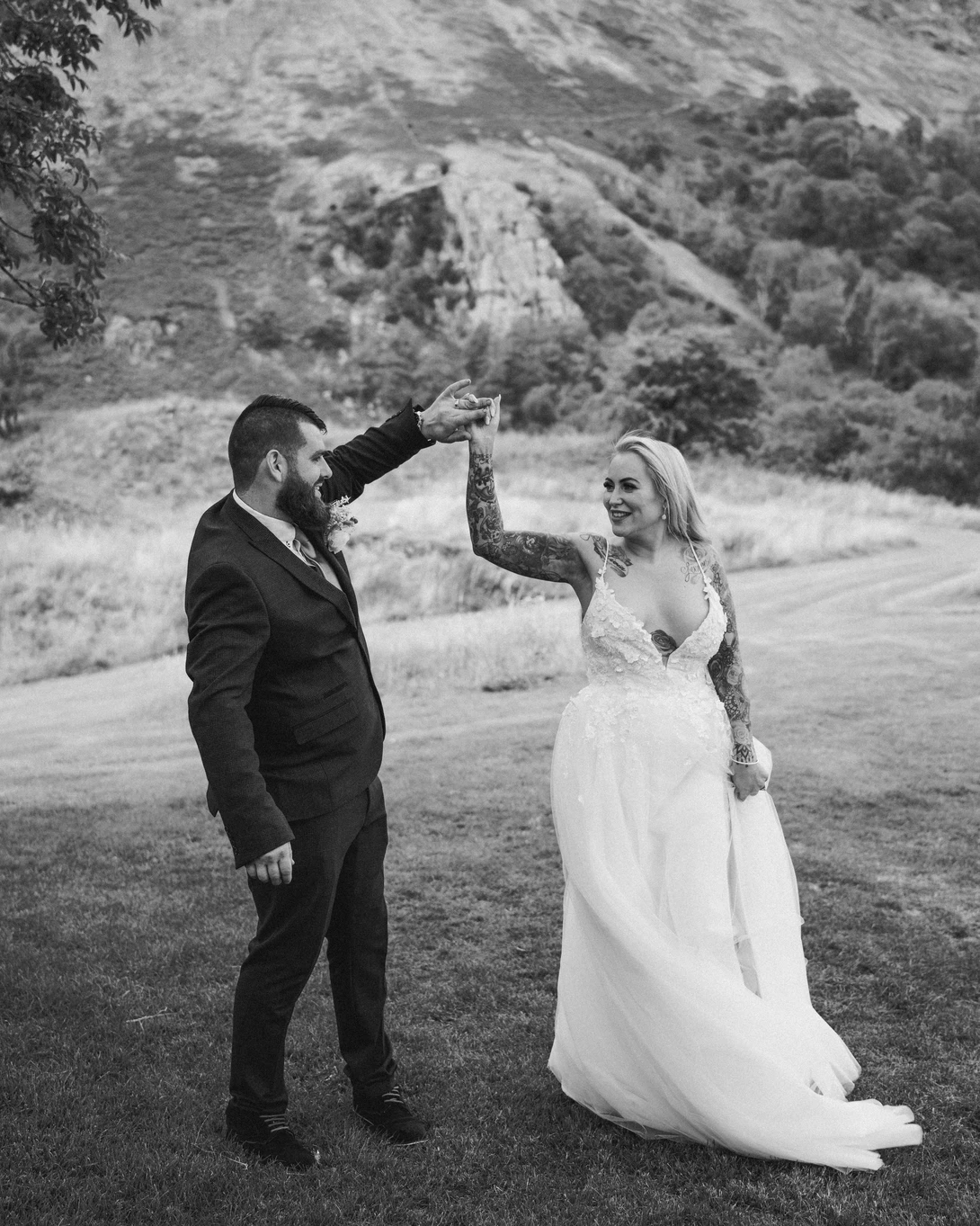 Bride and groom exchanging vows with hands raised in a mountainous outdoor setting.
