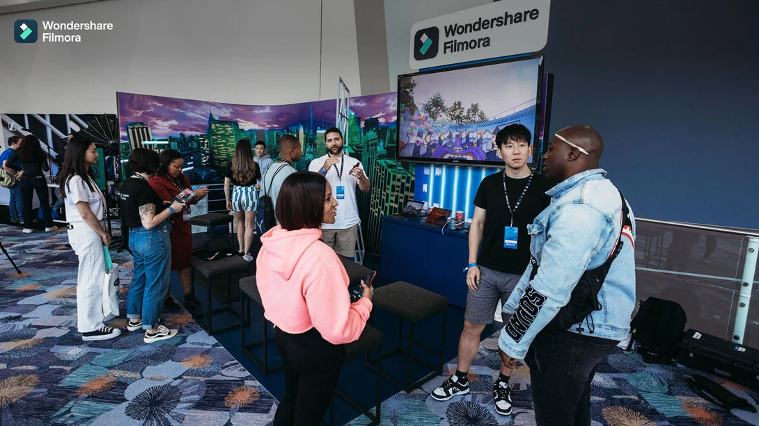 Attendees gather at a Wondershare Filmora booth at a convention, viewing video production displays and promotional materials.