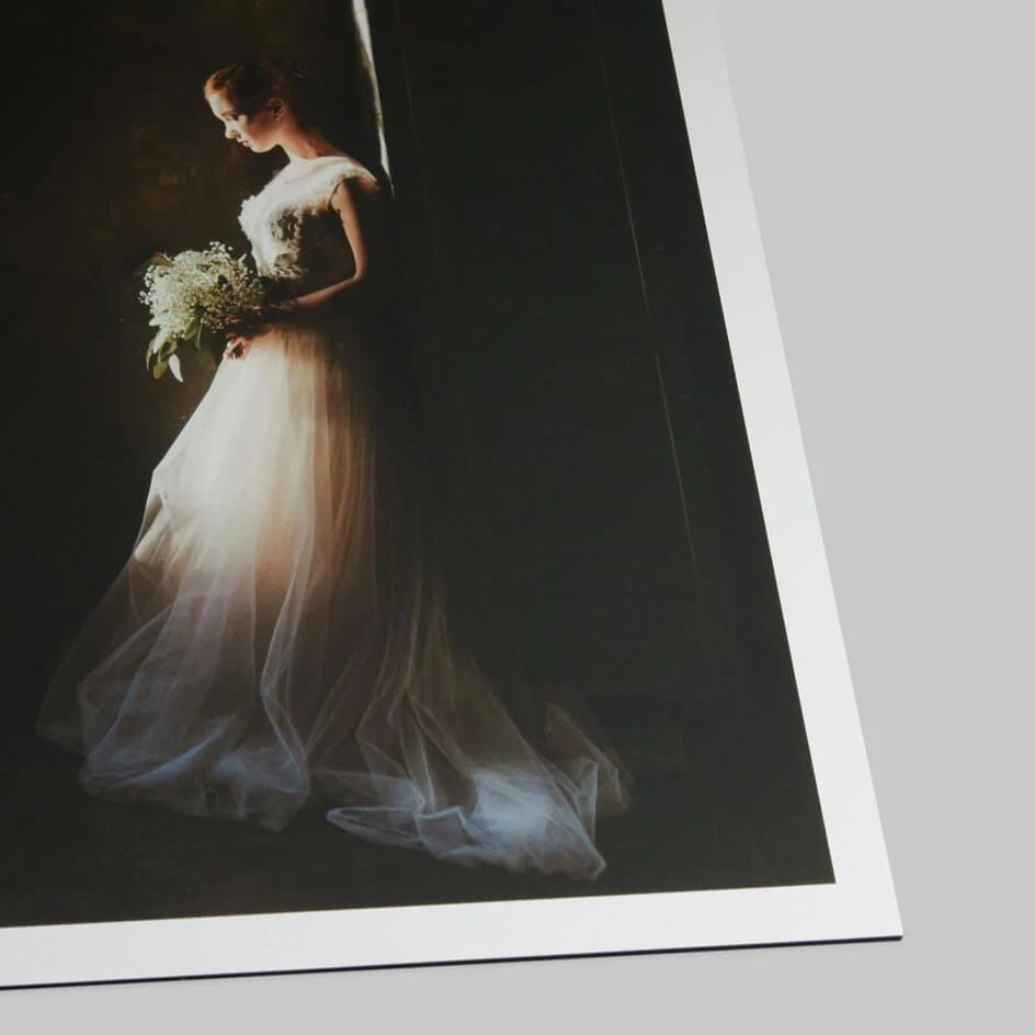 Bride in flowing white gown holding bouquet, photographed against dark backdrop with dramatic side lighting.