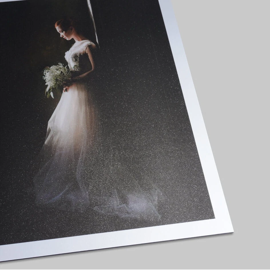 Printed wedding photograph showing a bride in a white gown holding a bouquet, backlit with dramatic lighting.