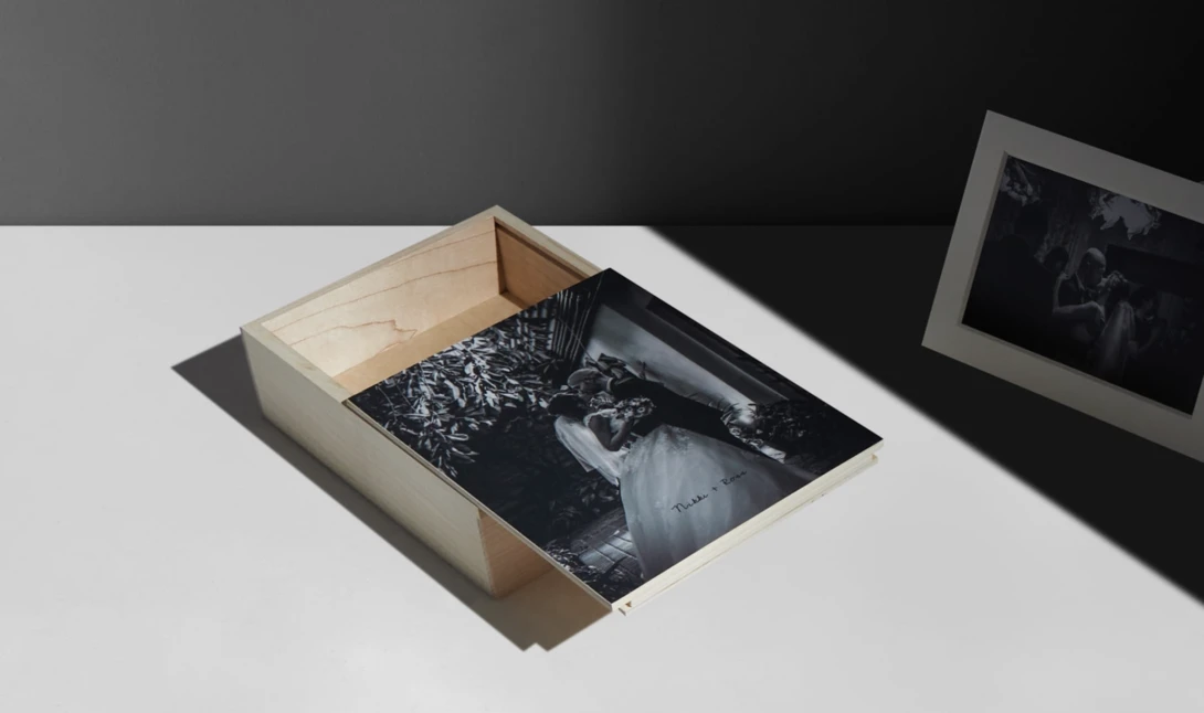 Wooden box containing a black and white photograph, displayed on white surface with dramatic side lighting.
