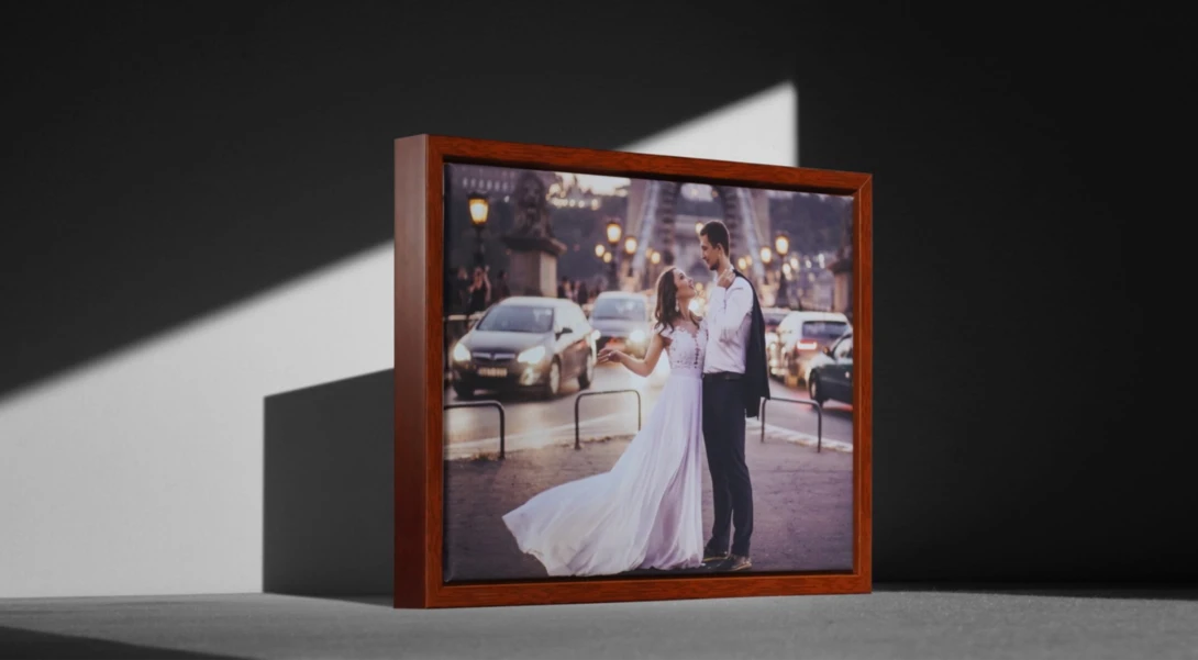 Framed wedding portrait displayed on a surface, showing a bride and groom outdoors with vehicles visible in the background.