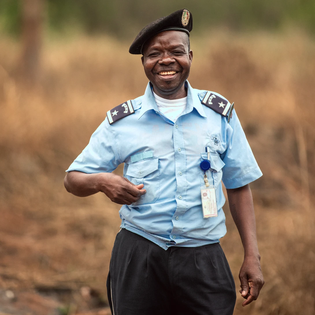 Smiling person in light blue uniform shirt with shoulder insignia standing outdoors.