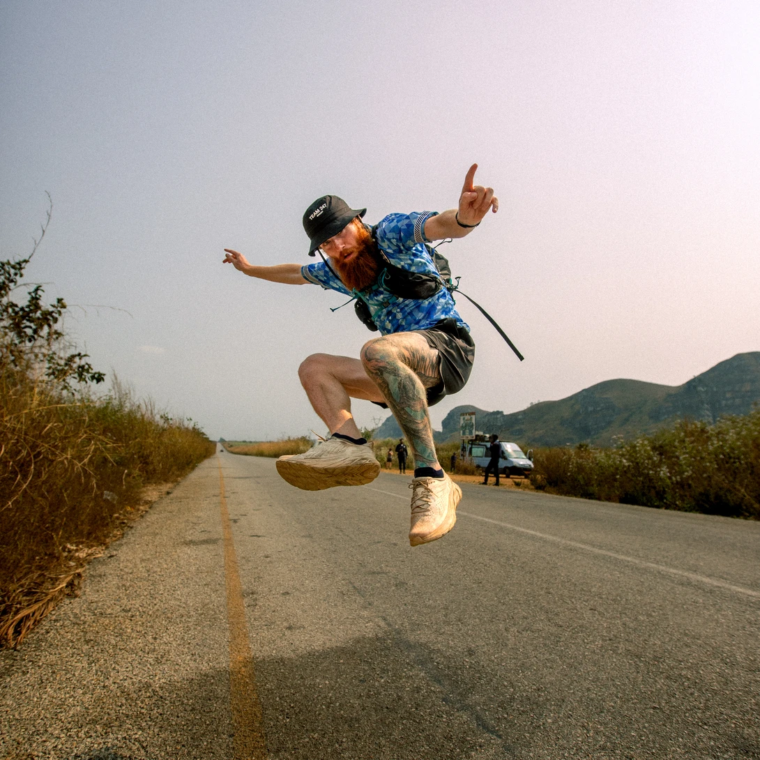 Skateboarder performing an aerial trick on a rural road at golden hour with mountains in the background.