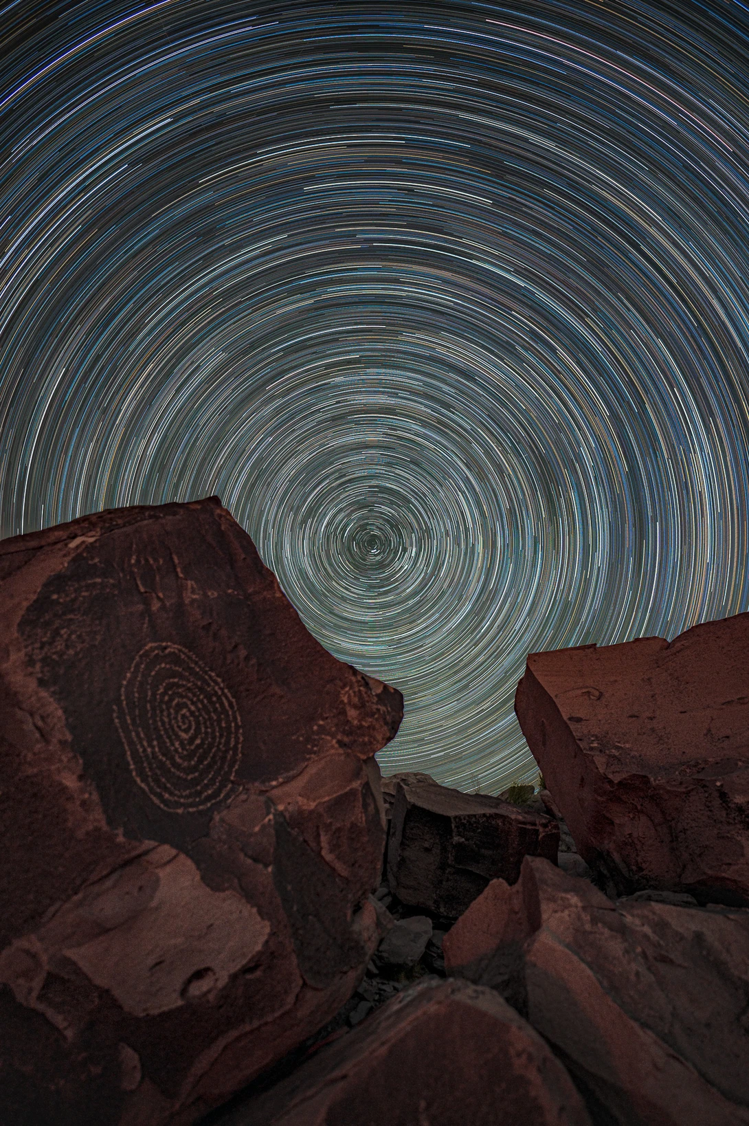 Star trail circles above red rock formations under a night sky.