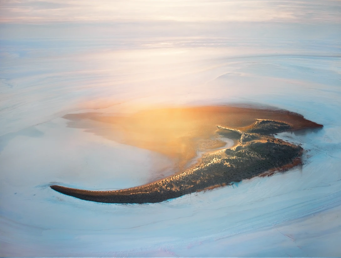 Aerial view of a crocodile-shaped landmass surrounded by misty water at sunrise.