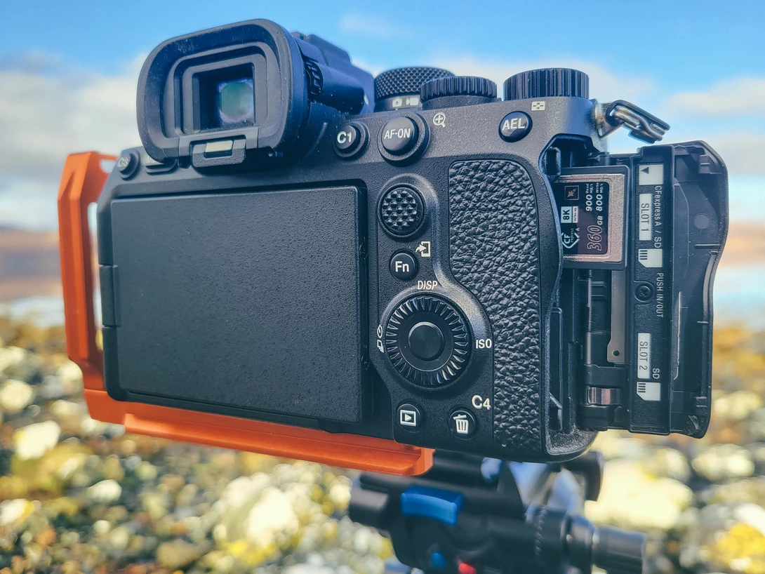 Professional mirrorless camera mounted on a tripod with articulating LCD screen deployed, showing rear controls and ports in outdoor daylight.
