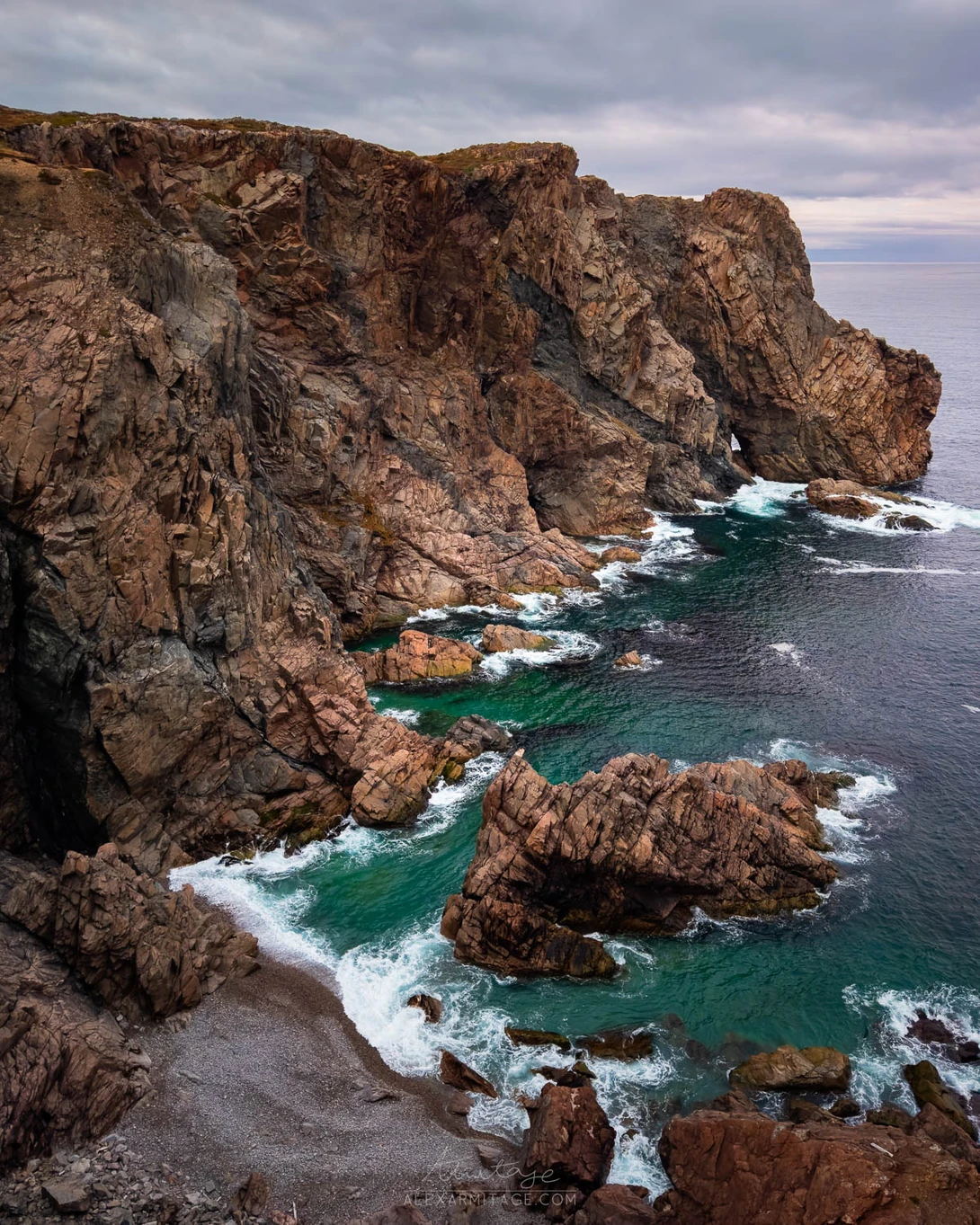 Dramatic rocky coastline with turquoise waves crashing against dark brown cliffs.