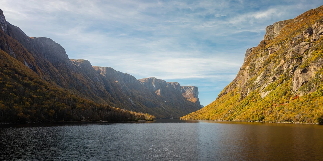 Steep mountain cliffs frame a calm alpine lake surrounded by autumn foliage.