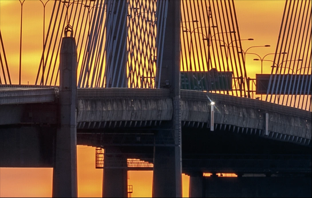 Modern bridge with geometric cable stays silhouetted against golden sunset sky.