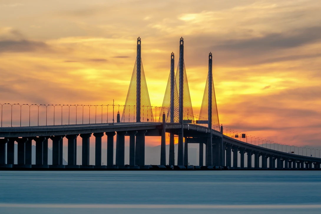 Cable-stayed bridge with four tall towers spanning a body of water at golden hour sunset.