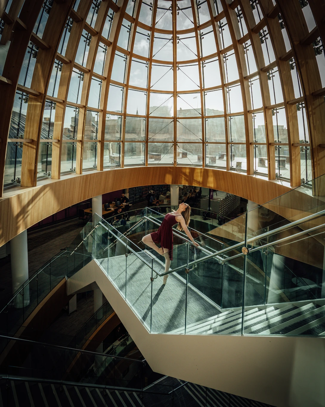 Woman descending curved staircase under geometric glass dome with dramatic natural light.