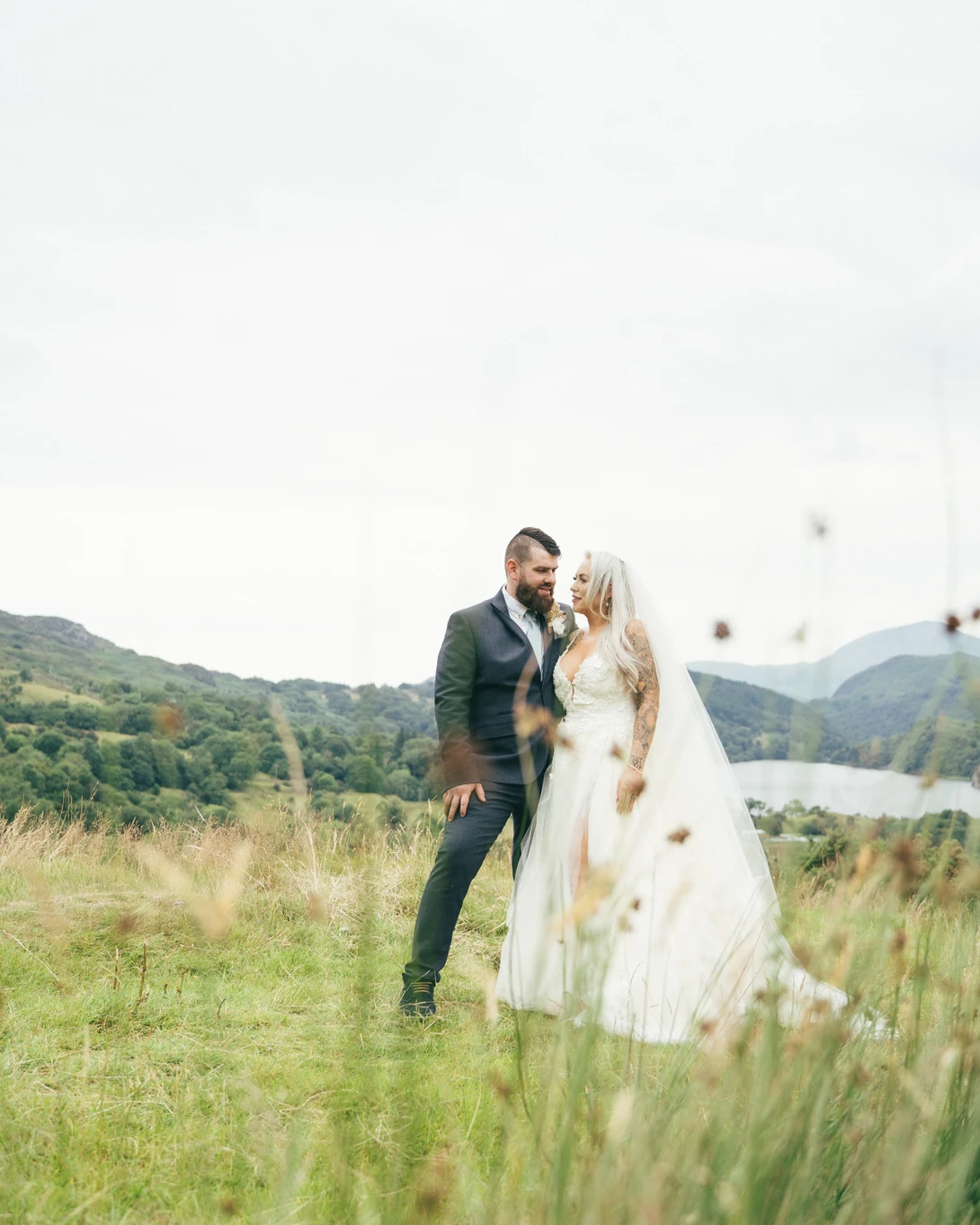 Bride and groom embrace in a grassy field with forested hills in the background.