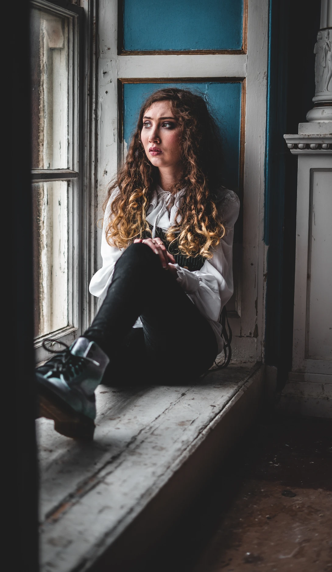 Woman with curly hair sitting in a doorway with blue wall behind her.