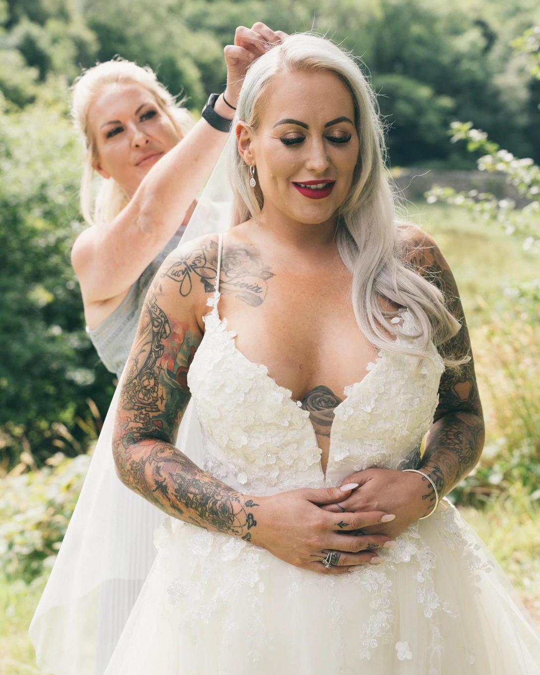 Two women in white wedding dresses in an outdoor garden setting during daytime.
