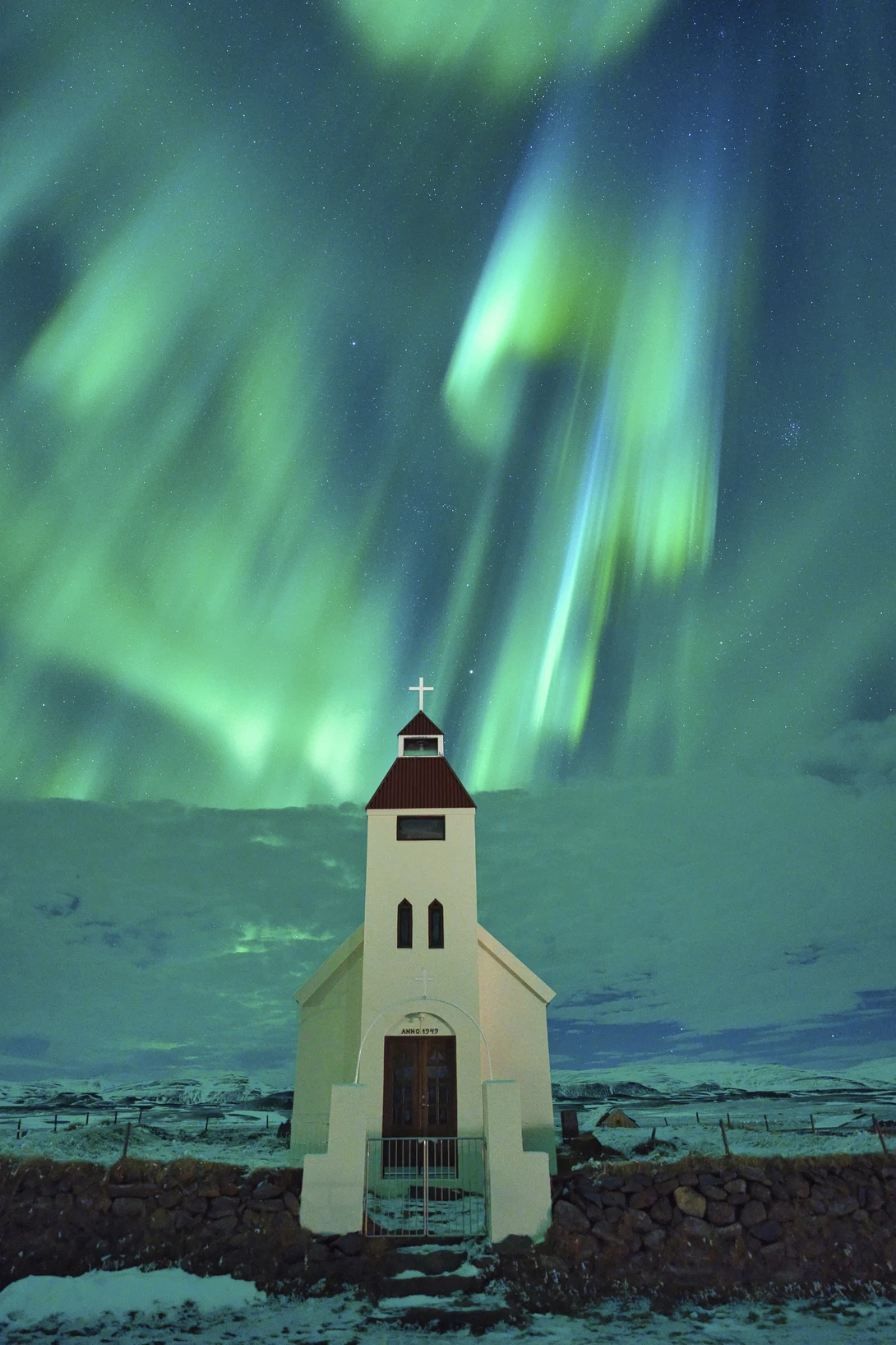 White wooden church building standing alone beneath aurora borealis dancing across night sky.
