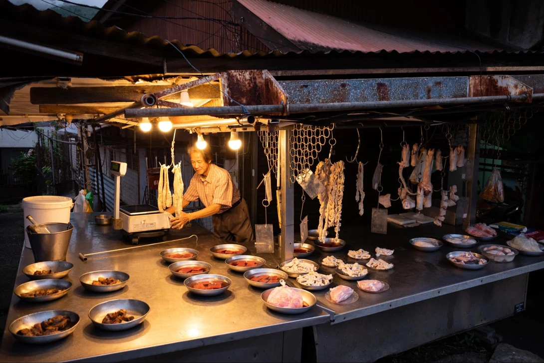 Museum diorama of a traditional butcher shop with figure, hanging meats, and display counter with prepared dishes.