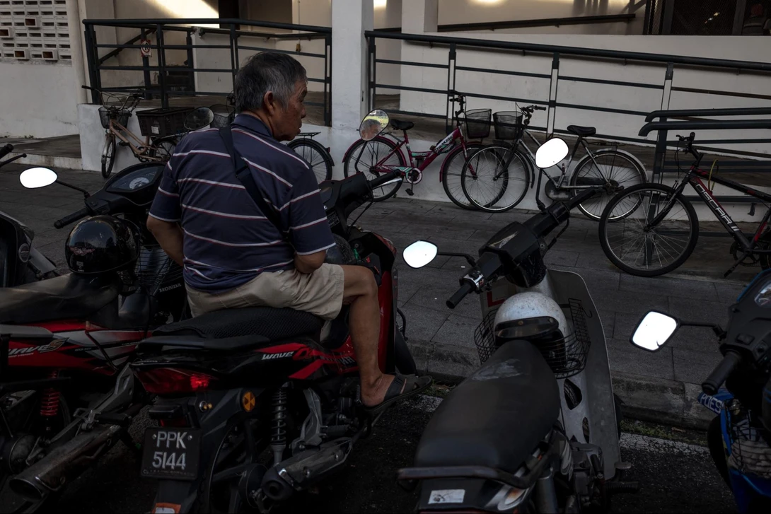 Man in striped polo shirt examining motorcycle with overhead studio lighting setup visible.