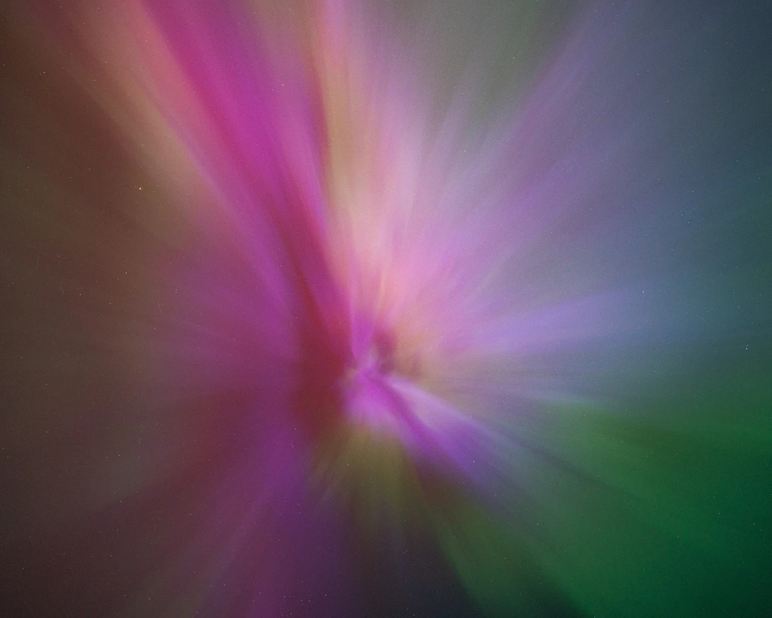 Abstract radial light burst with magenta, purple, and green rays emanating from center.