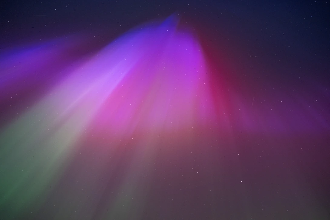 Abstract aurora-like light rays in magenta and green gradients against a dark starry background.