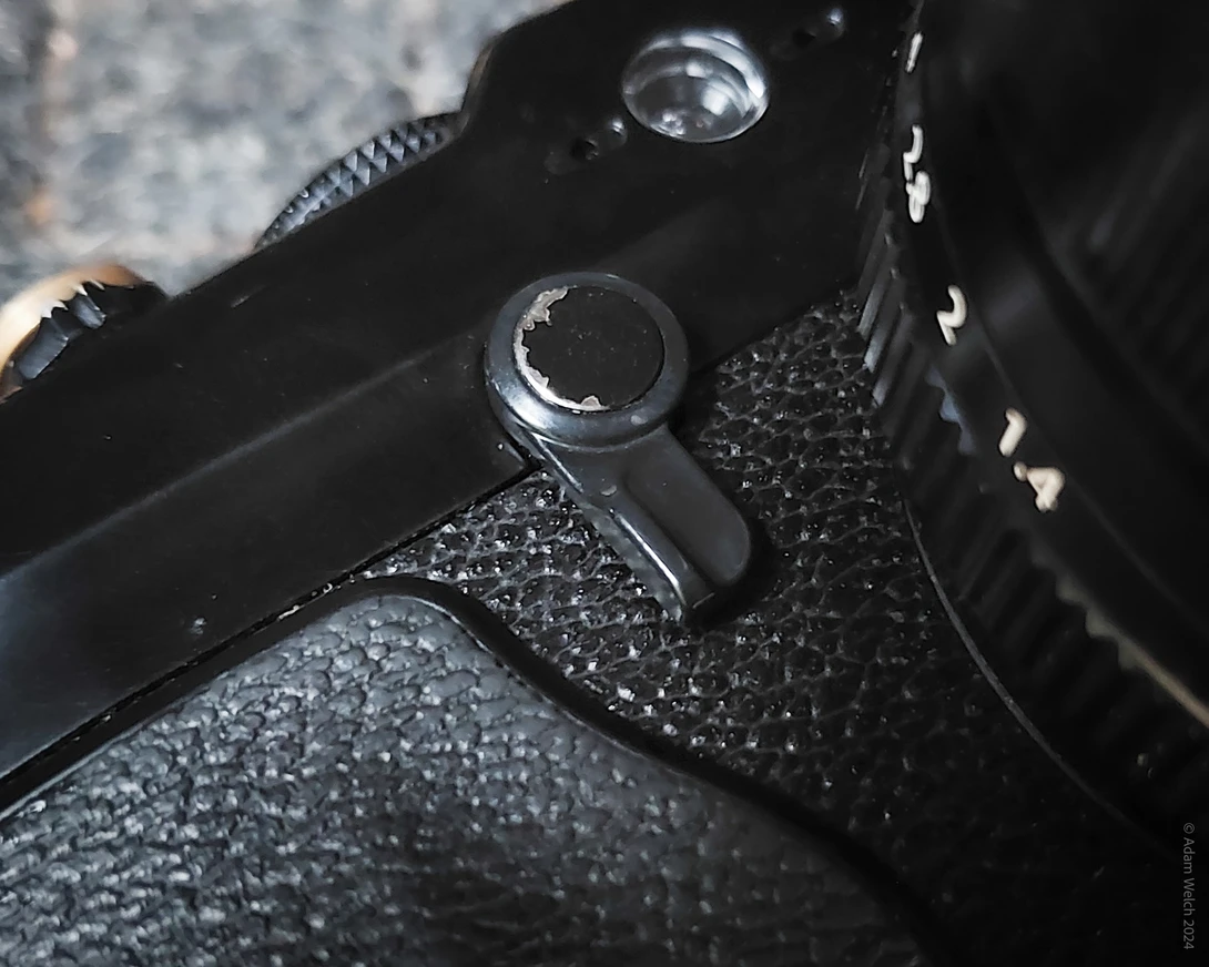 Close-up of camera body with water droplets on textured surface and metal controls.