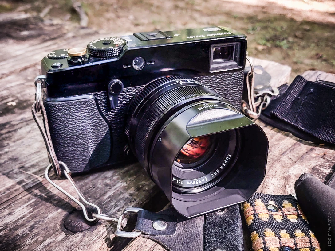 Black rangefinder camera with attached lens and shoulder strap on textured ground surface.