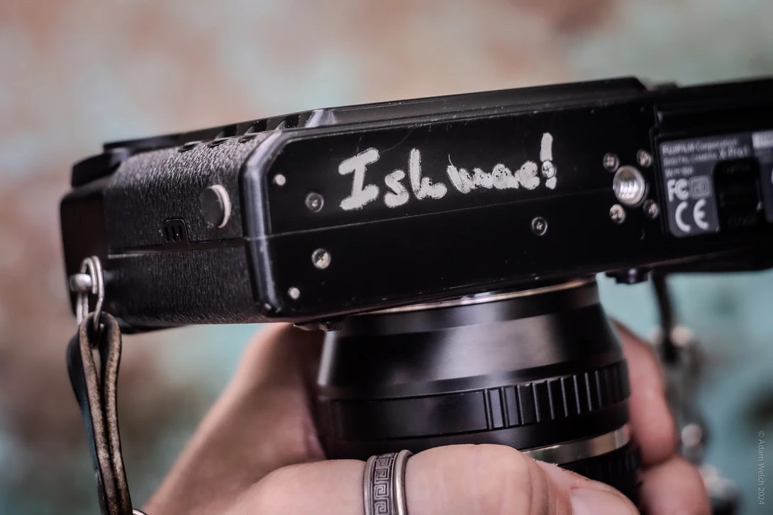 Close-up of a black rangefinder camera with handwritten text on the top plate, held in someone's hands.