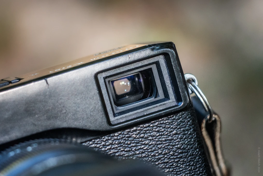 Close-up of a vintage rangefinder camera's viewfinder window and textured body with blurred background.